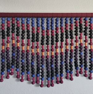 Photography of handmade bead art of many strings of purple and black beads hanging on a purple rod.